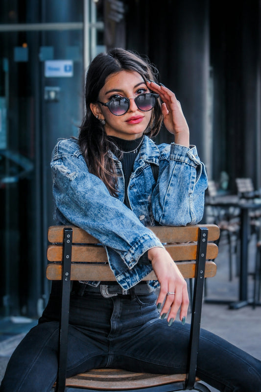 woman in blue denim jacket and black sunglasses sitting on brown wooden bench