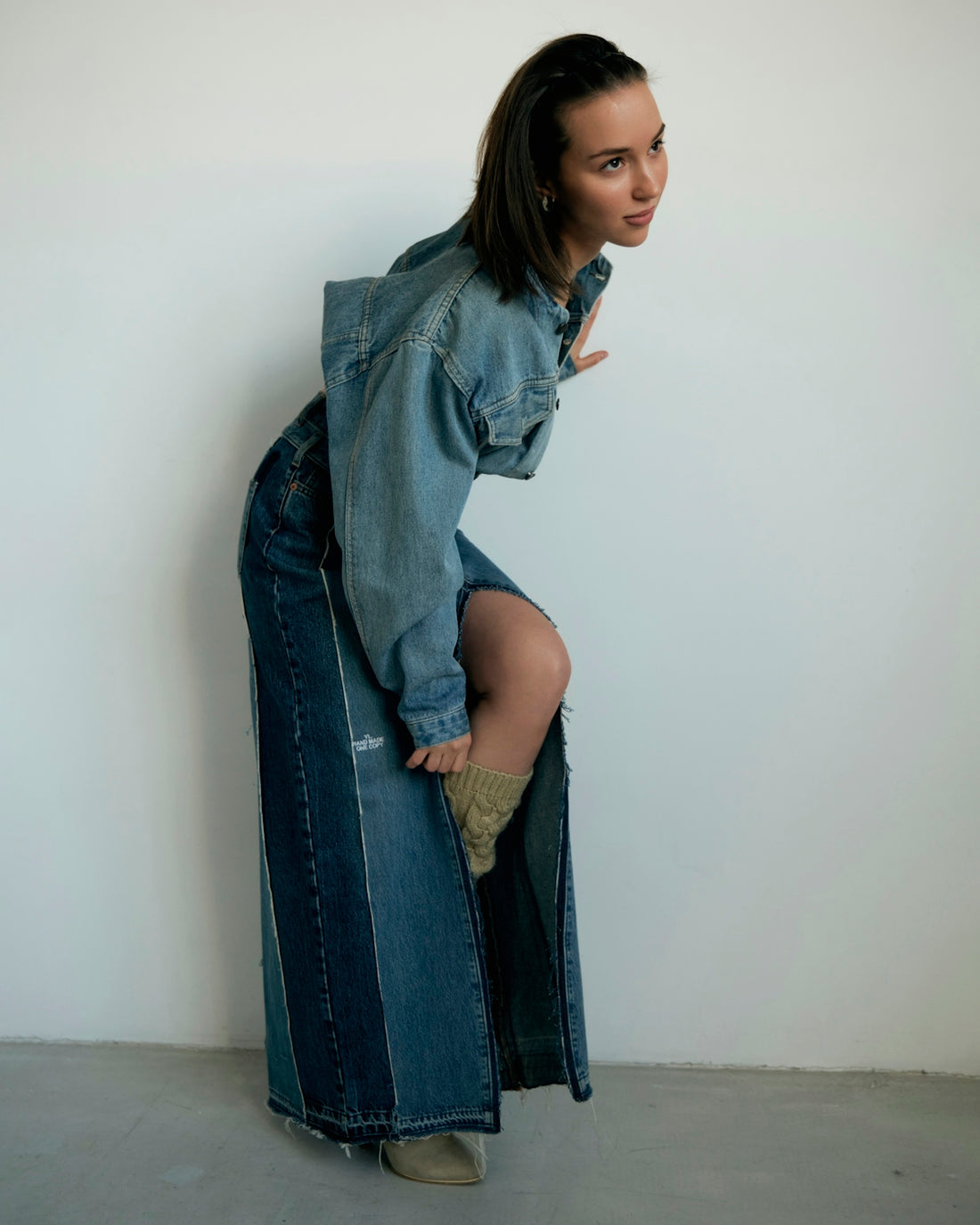 Woman poses in denim outfit next to a wall
