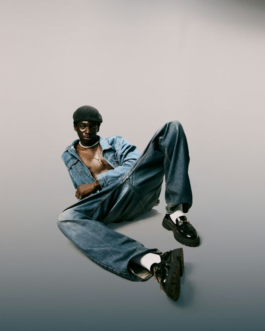 Man in denim outfit sits on a gradient background.
