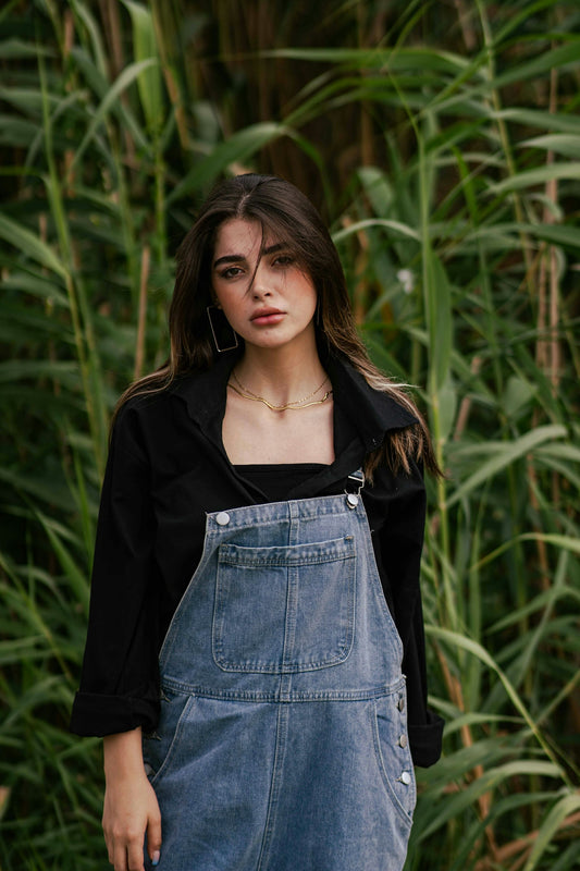 Young woman in denim overalls standing near tall grass