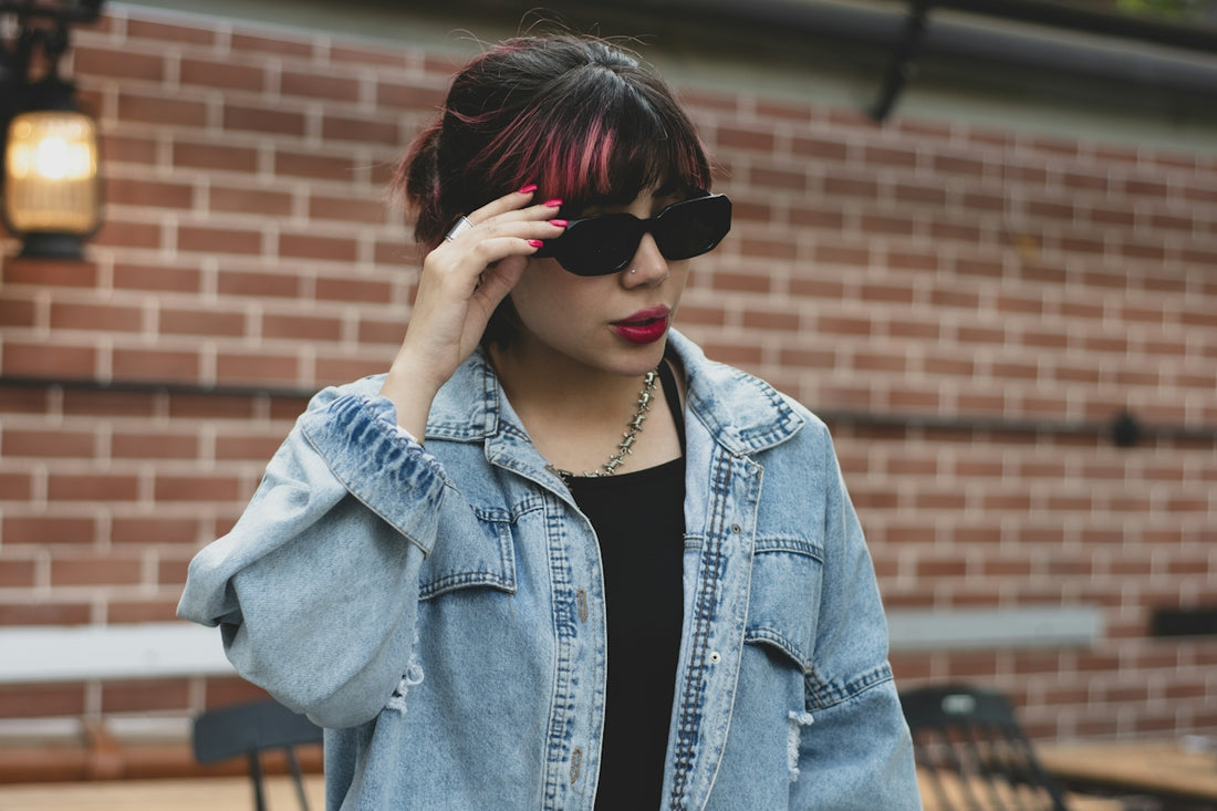 Woman in denim jacket adjusts sunglasses outdoors