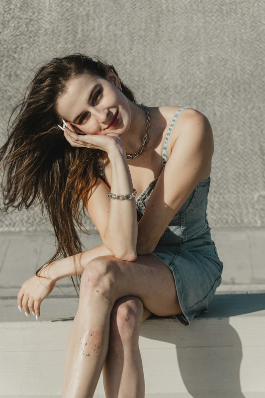 Young woman in denim dress smiles, resting chin on hand.