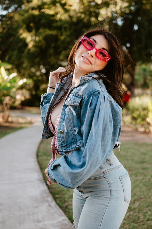 A young woman wearing sunglasses and denim jacket outdoors