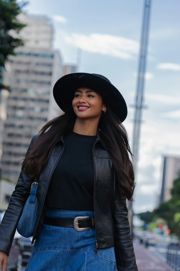 A woman in a hat and leather jacket walks outdoors