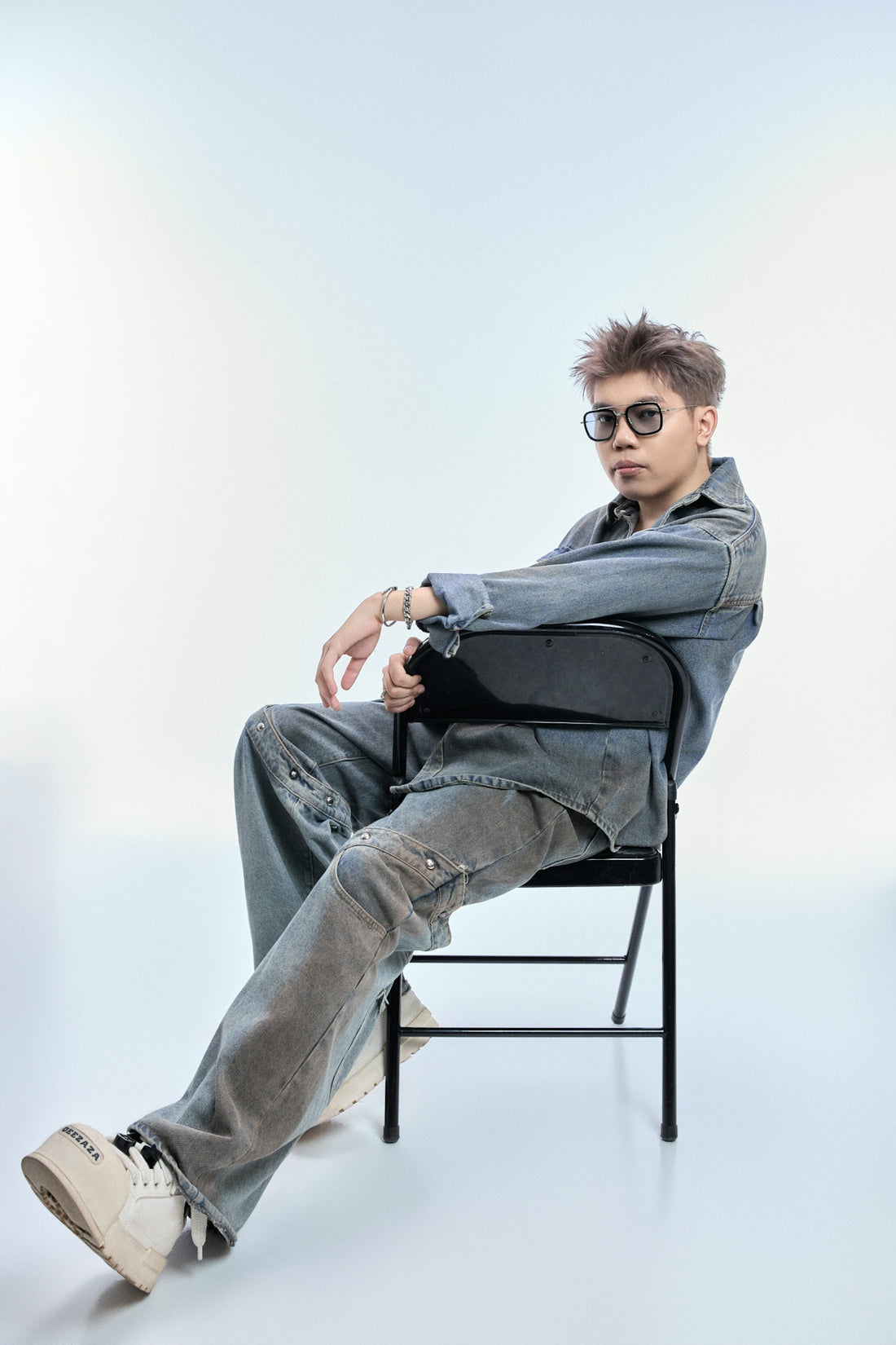 Man in denim outfit sitting on chair with sunglasses.