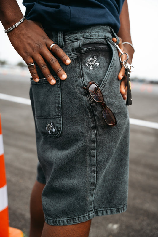 Person wearing dark denim shorts with sunglasses in pocket.