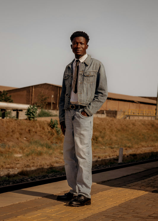A young man in denim stands on a train platform.