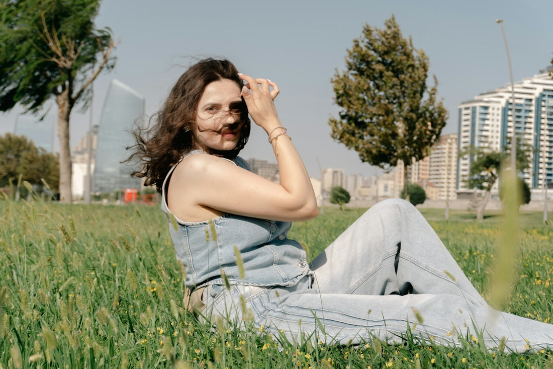 Woman in denim sitting in green field with city view