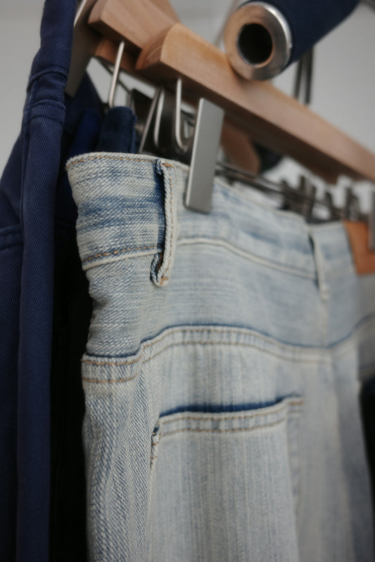 Light blue denim jeans hanging on a wooden hanger.