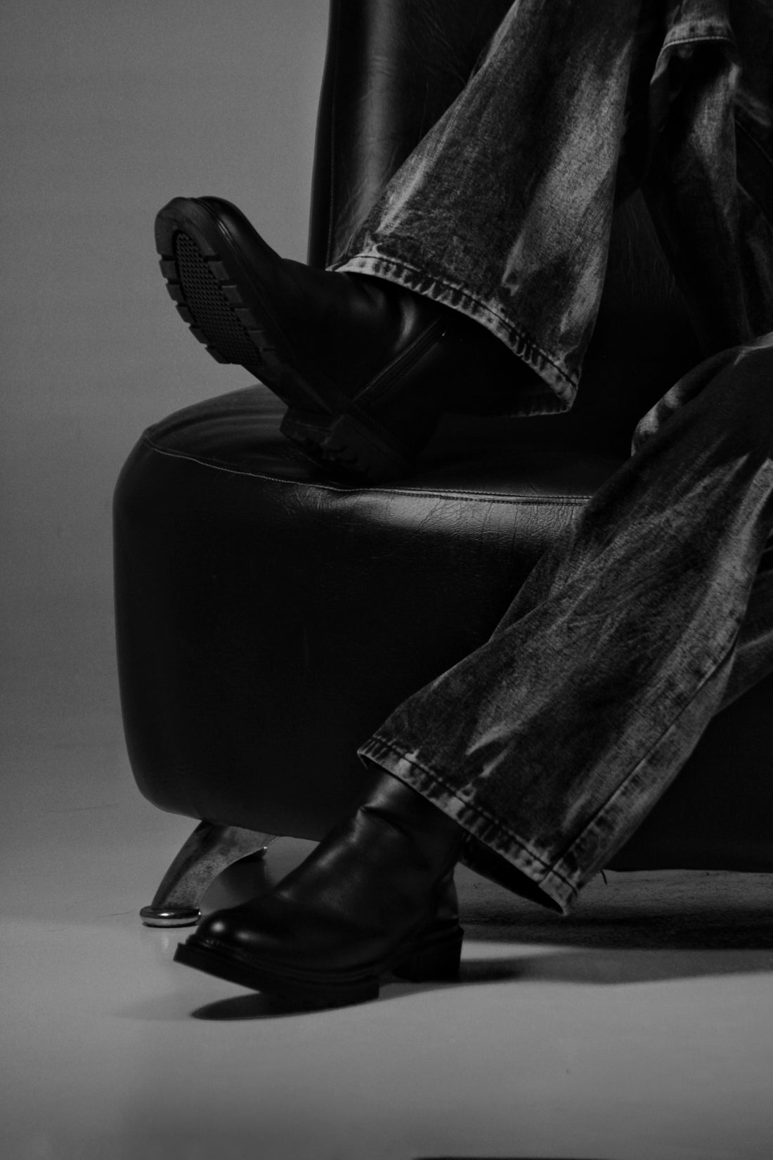 A person in denim jeans and black boots on a leather chair