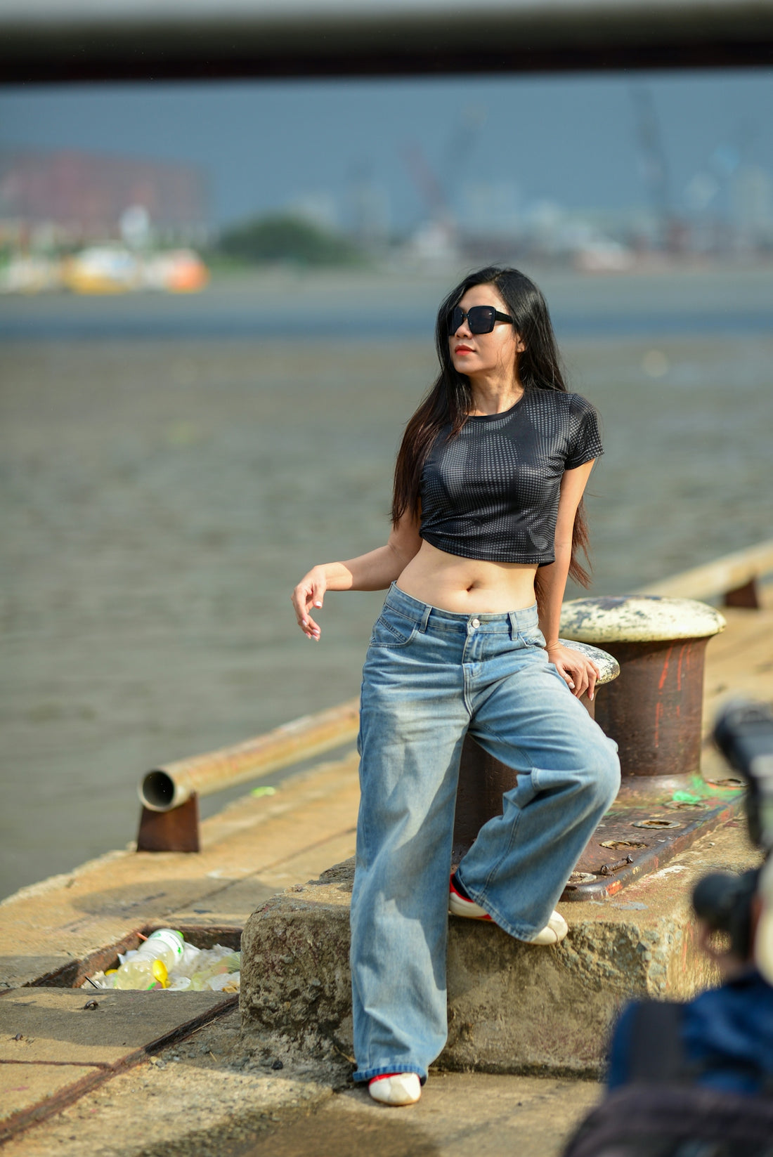 A woman in a black crop top and jeans leaning against a dock bollard