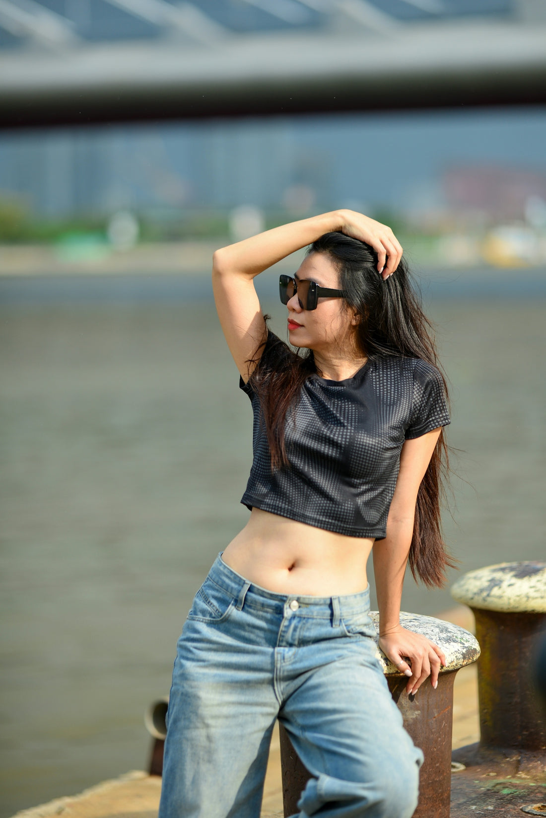 A woman in a black crop top and jeans leaning against a bollard